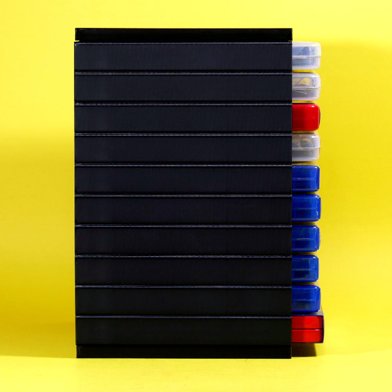 A stack of black rectangular plastic cases or trays with clear lids, shown standing upright against a bright yellow background. Several clear-lidded ends are visible on the right side, revealing red and blue items inside.