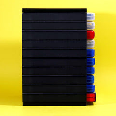 A stack of black rectangular plastic cases or trays with clear lids, shown standing upright against a bright yellow background. Several clear-lidded ends are visible on the right side, revealing red and blue items inside.