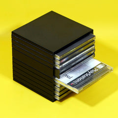 A black plastic CD stackable drive case holding several PlayStation CDs, with one PlayStation CD pulled out, set against a bright yellow background.