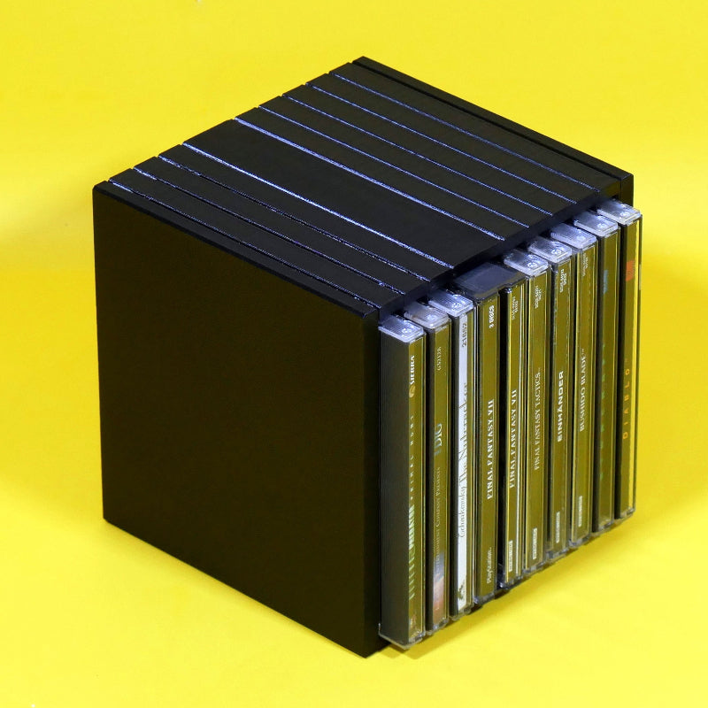 A black cube-shaped CD case holding multiple CD cases, photographed on a bright yellow background.
