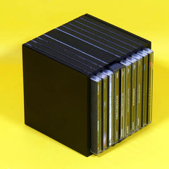 A black cube-shaped CD case holding multiple CD cases, photographed on a bright yellow background.