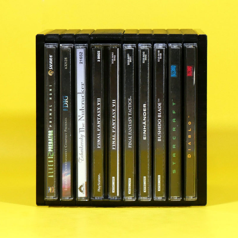 A black plastic multi-disc game case holding multiple PlayStation game discs, photographed against a bright yellow background. Visible game titles include Predator, The Nighthawk, Final Fantasy VII, Final Fantasy VIII, Einhänder, Bushido Blade, Striscart, and Diablo.