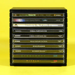 A black plastic multi-disc game case stack holding multiple PlayStation game cases, photographed against a solid bright yellow background. Visible game titles include Alien, Predator, Dig, Cthulhu Conspiracy, Final Fantasy VII, Final Fantasy Tactics, Einhänder, Bushido Blade, Starcraft, and Diablo.